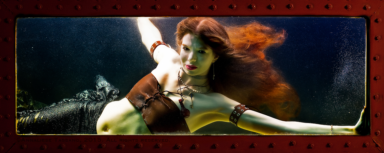 A white mermaid with long red hair floating behind her and brown leather, steampunk costume.