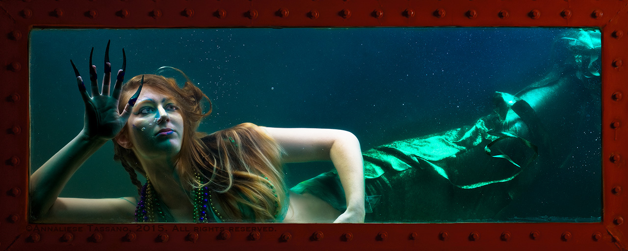 Green tailed mermaid claws the window of the tank in which she is imprisoned.
