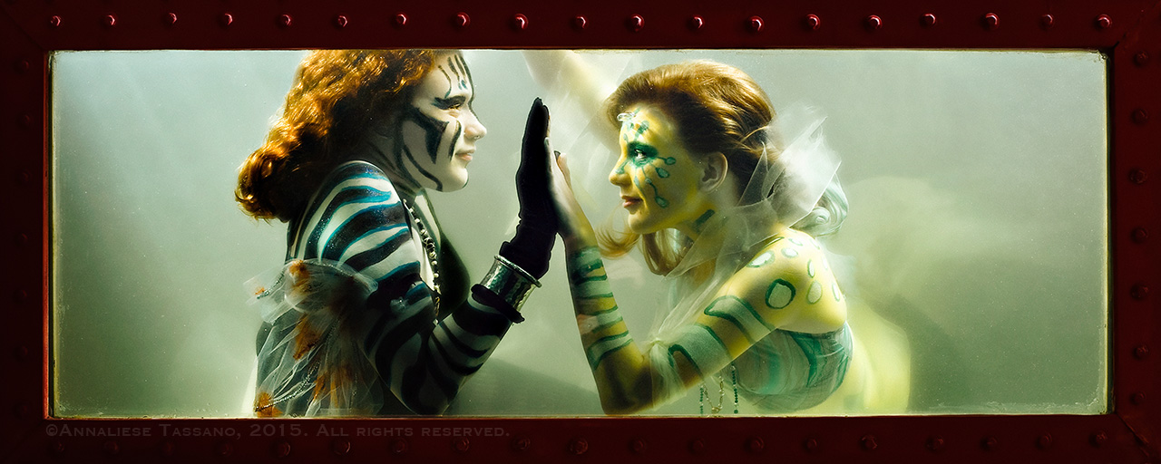 Two sister mermaids look at one another pressing palms together.