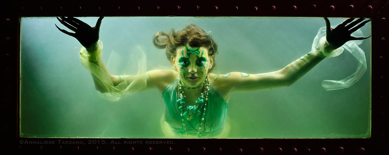 A creepy young mermaid with claws and exotic marking stares out the window of her tank.