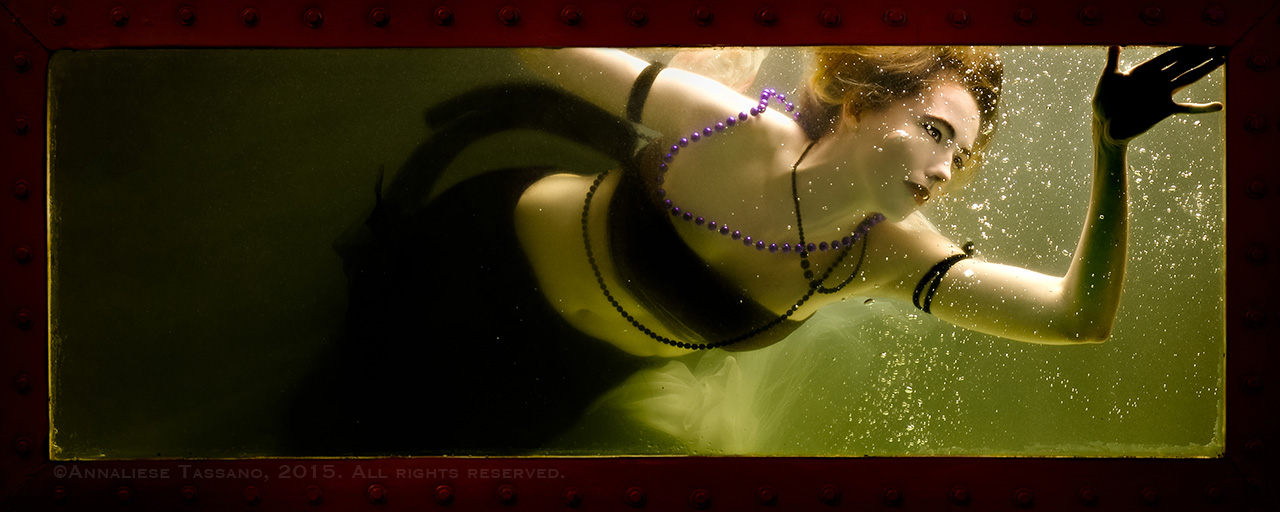 A short haired brunette mermaid swims by a window of her tank.