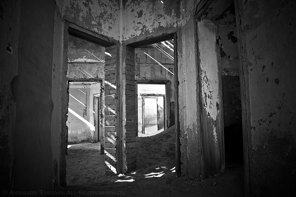 A black and white view of many doors in one of the many sand filled buildings found in Kolmanskop, once a thriving diamond mining community in the Namib Desert of Namibia.