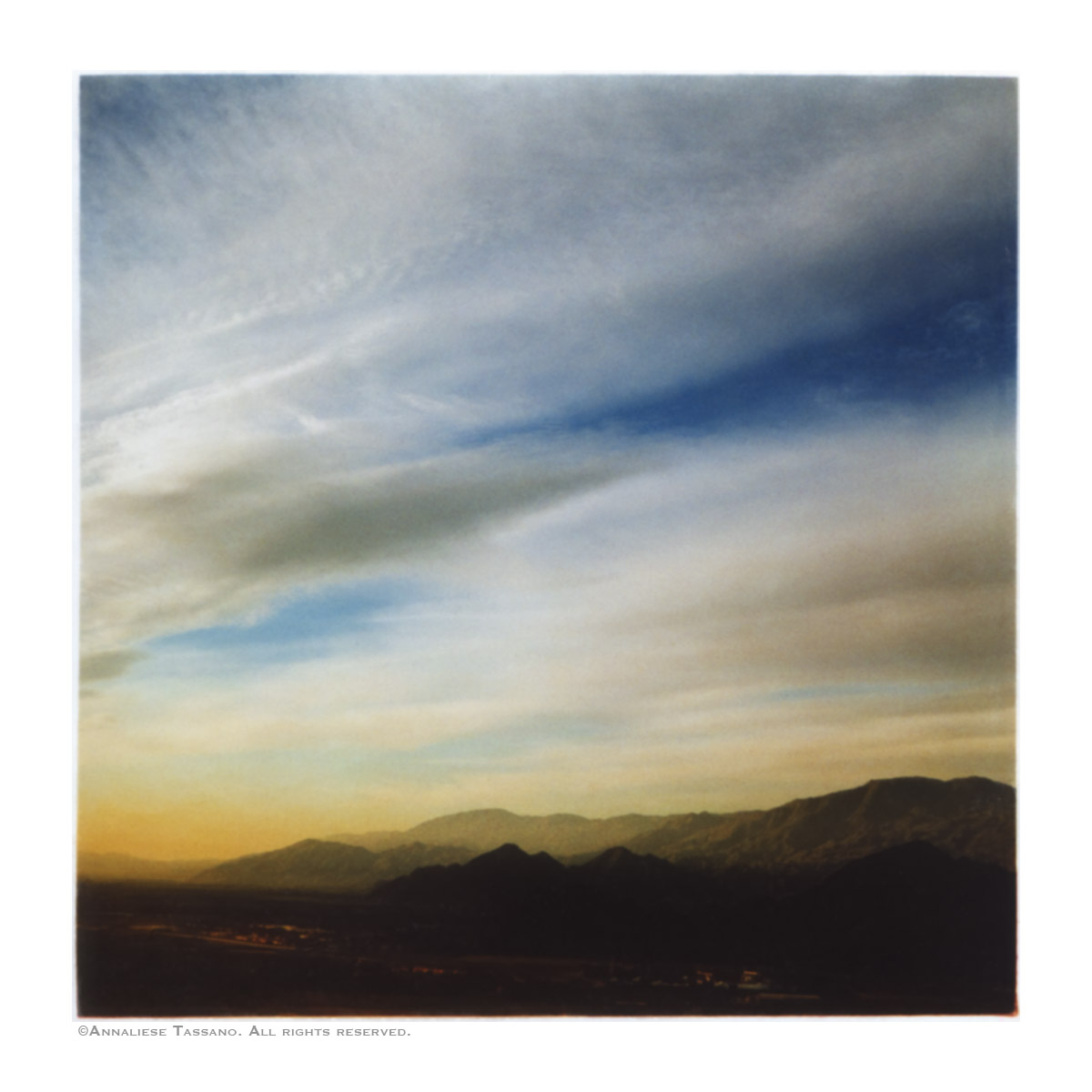 A high view of the desert floor, a cloudy sky, and sunrise on the mountains surrounding Palm Springs, Califonia.