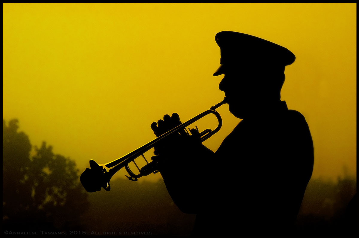 The silhouette of a military trumpeter playing taps in front of a yellow dawn sky at a September 11, 2002 memorial.