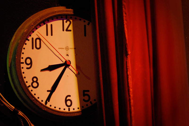 A General Electric analogue clock face side stage and partly obscured by a red curtain reads 8:35 at Portland, Oregon's Aladdin Theater.