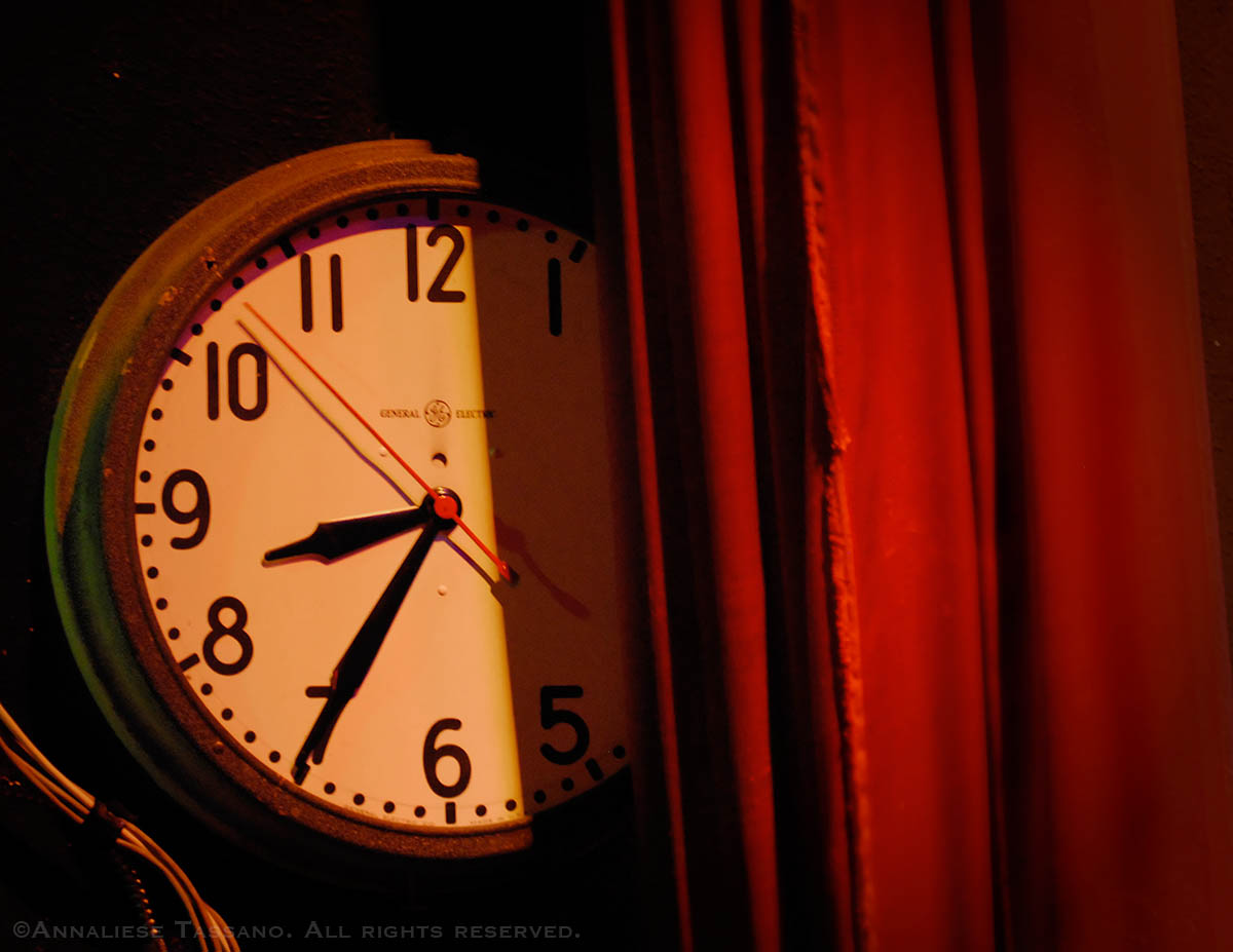 A General Electric analogue clock face side stage and partly obscured by a red curtain reads 8:35 at Portland, Oregon's Alddin Theater.