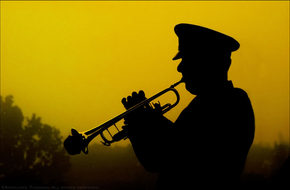 The silhouette of a military trumpeter playing taps in front of a yellow dawn sky at a September 11, 2002 memorial.