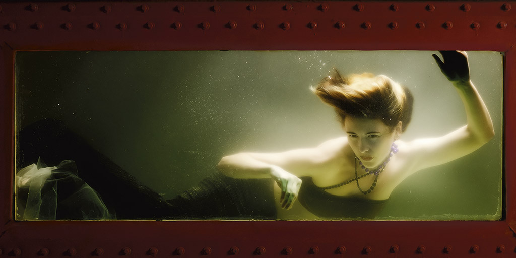 A fair skinned mermaid with short brown hair is confined in a tank.