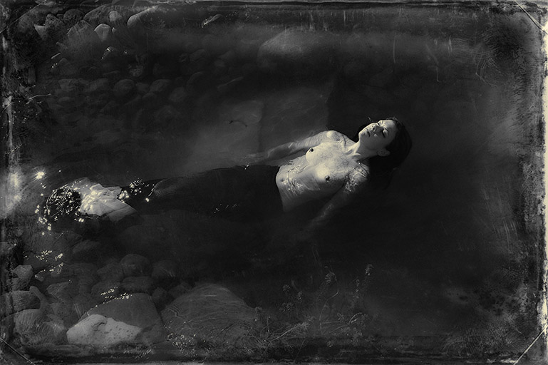 Seen in a victorian style photograph, a mermaid relaxes, floating in her pond.